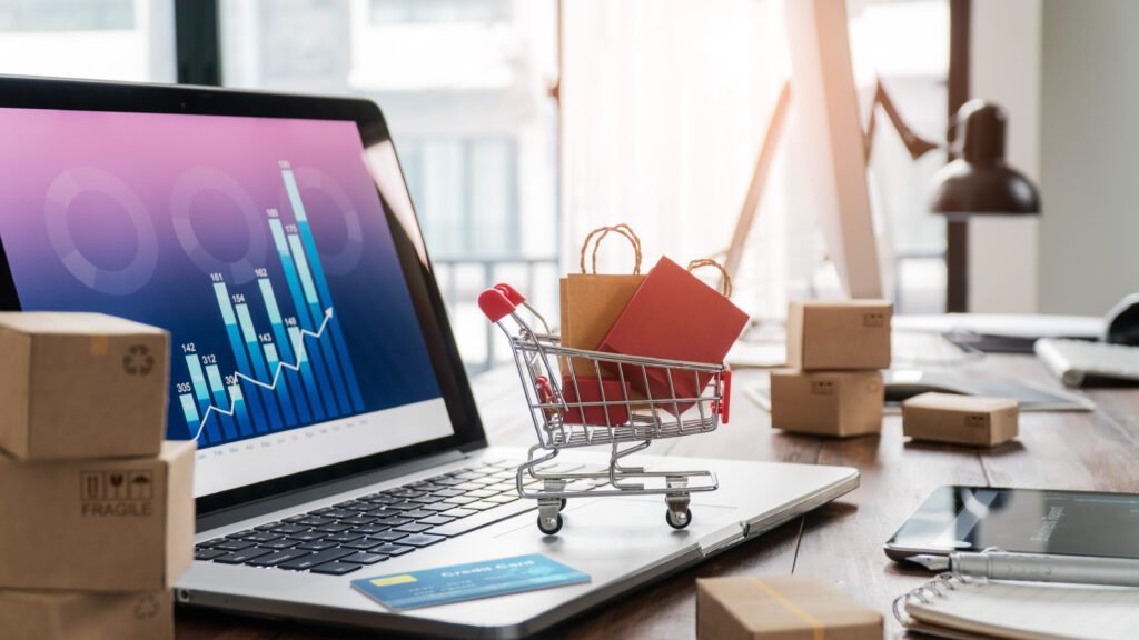 Sacs d'épicerie dans un panier et carte de crédit sur un ordinateur portable avec des boîtes en papier sur une table et un graphique de croissance économique sur un écran, achat et vente de services en ligne sur un réseau, concept d'achat en ligne et de commerce électronique.