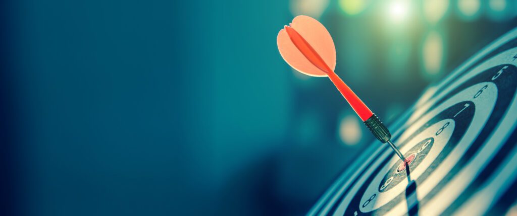 La cible ou le plateau de fléchettes a une flèche rouge qui frappe le centre d'un tir pour les concepts d'affaires de ciblage et d'objectifs gagnants.